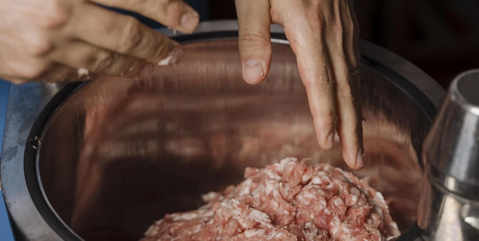 Mani che lavorano carne macinata fresca in contenitore d’acciaio