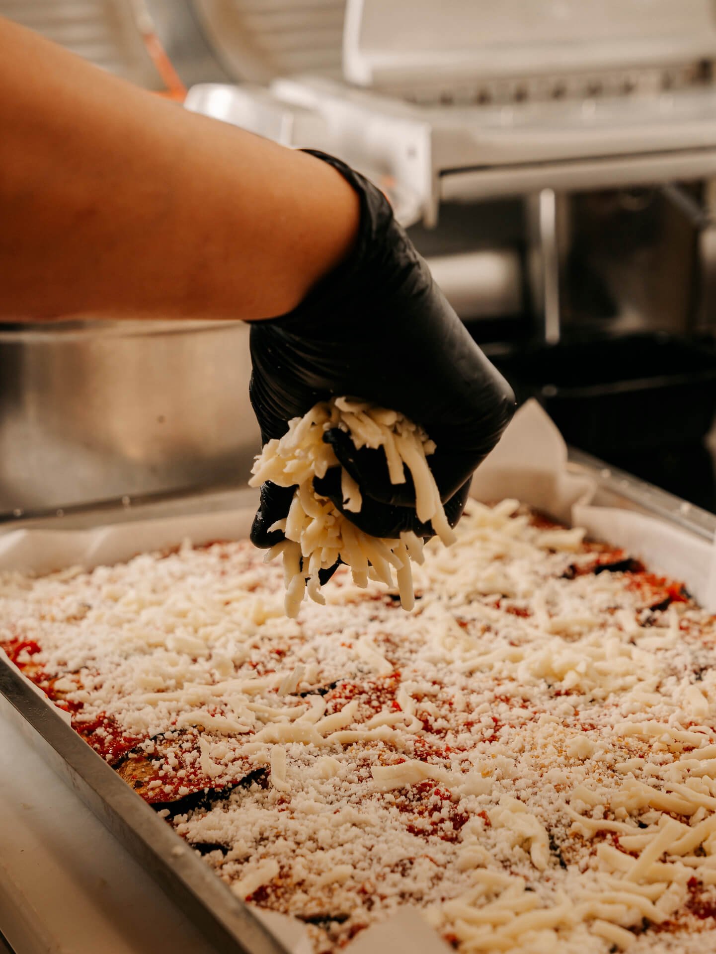 aggiunta-formaggio-parmigiana-preparazione-spacciocarlopoma Aggiunta di formaggio sulla parmigiana nel laboratorio Carlo Poma